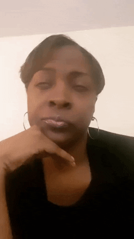 A Woman With Her Hand On Her Chin Is Wearing Hoop Earrings And A Black Shirt . GIF