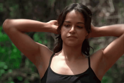 A Woman With Her Hands Behind Her Head Looks At The Camera GIF