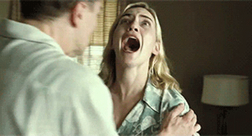 A Woman With Her Mouth Open Is Being Held By A Man In A Room . GIF