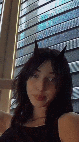 A Woman With Horns On Her Head Is Taking A Selfie In Front Of A Window GIF