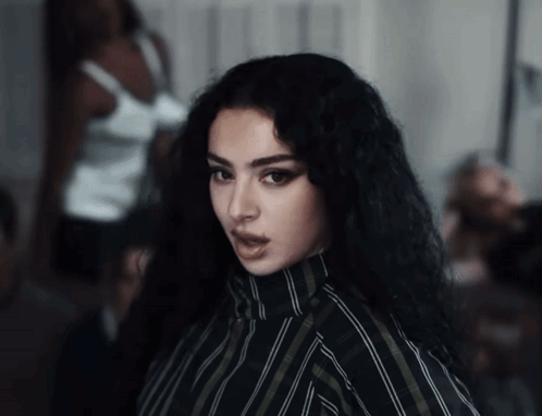 A Woman With Long Black Hair And A Striped Shirt Looks At The Camera GIF