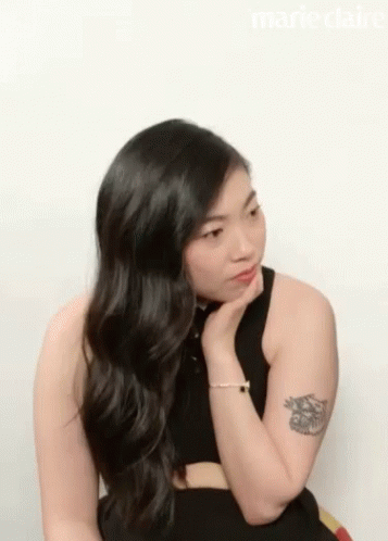 A Woman With Long Black Hair And A Tattoo On Her Arm Is Wearing A Black Top . GIF
