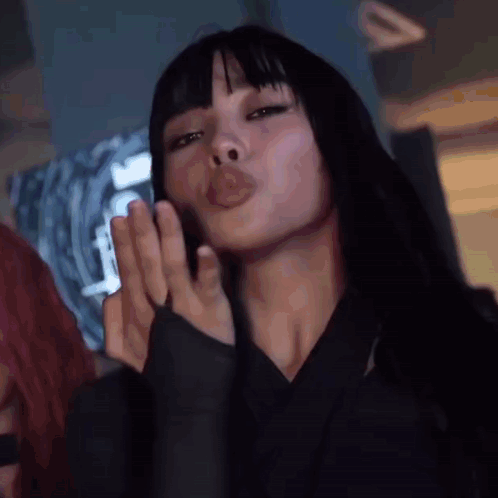 A Woman With Long Black Hair And Bangs Is Blowing A Kiss . GIF