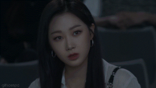 a woman with long black hair and hoop earrings is sitting in a dark room and looking at the camera .