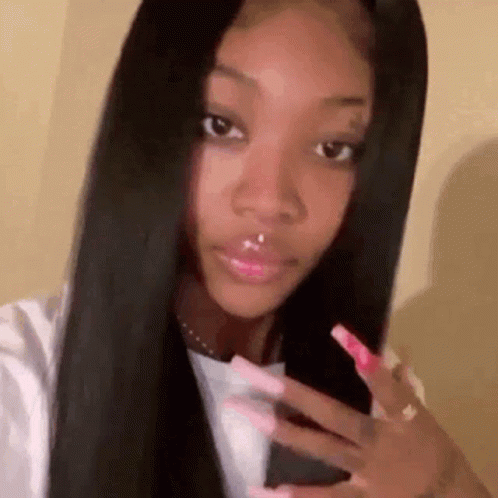 a woman with long black hair and long pink nails is taking a selfie .