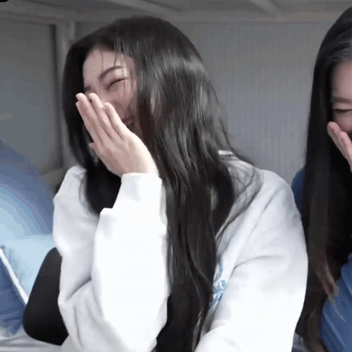 A Woman With Long Black Hair Is Laughing With Her Hands Over Her Mouth GIF