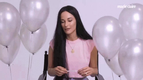 A Woman With Long Black Hair Is Sitting In A Chair Surrounded By Balloons . GIF