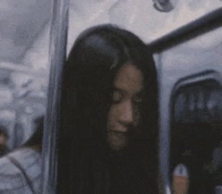 A Woman With Long Black Hair Is Sitting On A Bus And Looking At The Camera . GIF
