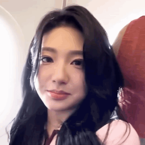 A Woman With Long Black Hair Is Sitting On An Airplane And Smiling . GIF
