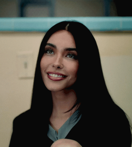 A Woman With Long Black Hair Is Smiling And Looking At The Camera GIF