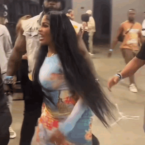 A Woman With Long Black Hair Is Standing In A Crowd . GIF