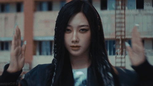 A Woman With Long Black Hair Is Standing In Front Of A Building With Her Hands In The Air GIF
