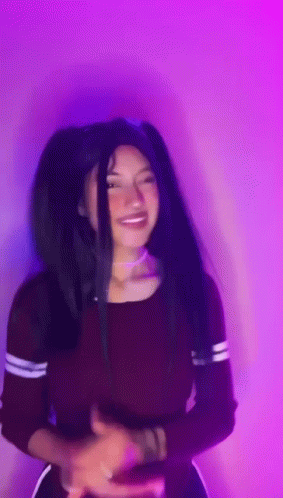 A Woman With Long Black Hair Is Standing In Front Of A Purple Wall . GIF