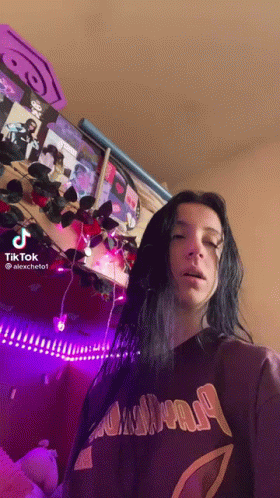 A Woman With Long Black Hair Is Standing In Front Of A Wall With Purple Lights . GIF