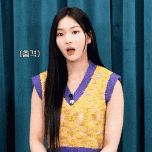 A Woman With Long Black Hair Is Wearing A Purple And Yellow Vest . GIF