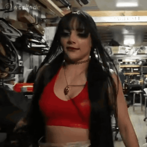 A Woman With Long Black Hair Is Wearing A Red Crop Top And Choker Necklace . GIF