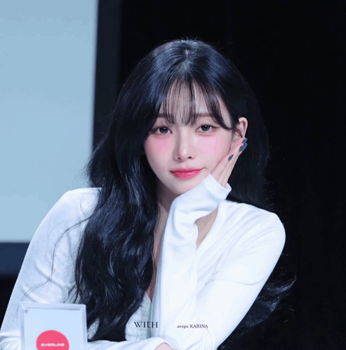 A Woman With Long Black Hair Is Wearing A White Shirt That Says Karina GIF