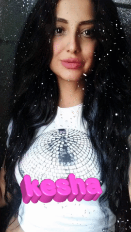 A Woman With Long Black Hair Is Wearing A White Shirt With The Word Kesha On It GIF