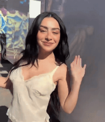 A Woman With Long Black Hair Is Wearing A White Tank Top And Smiling GIF