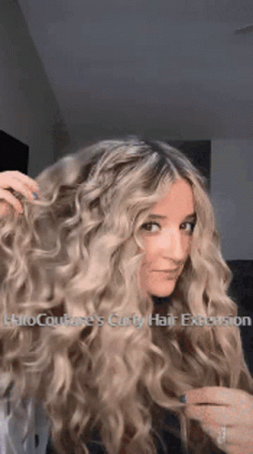A Woman With Long Blonde Curly Hair Has A Halo Couture 'S Curly Hair Extension In Her Hair . GIF