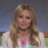 A Woman With Long Blonde Hair And A White Jacket Is Smiling . GIF
