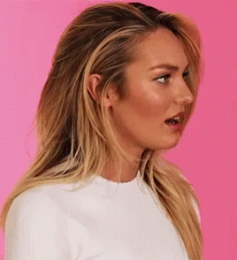 A Woman With Long Blonde Hair And A White Shirt Is Making A Funny Face . GIF