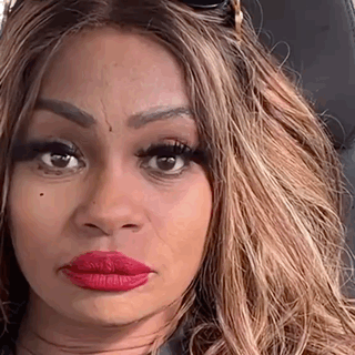 a woman with long blonde hair and red lipstick is sitting in a car and making a funny face .