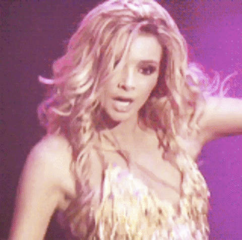 A Woman With Long Blonde Hair Is Dancing On A Stage In A Gold Dress . GIF
