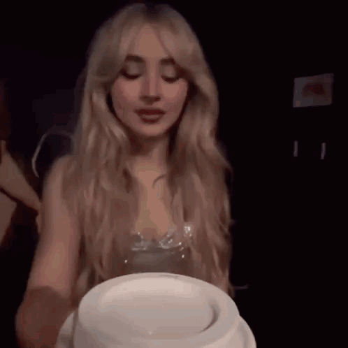 A Woman With Long Blonde Hair Is Holding A White Plate In Front Of Her Face . GIF