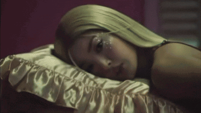 A Woman With Long Blonde Hair Is Laying On A Bed GIF