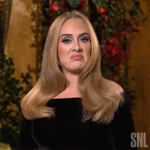 A Woman With Long Blonde Hair Is Making A Funny Face While Standing In Front Of Flowers . GIF