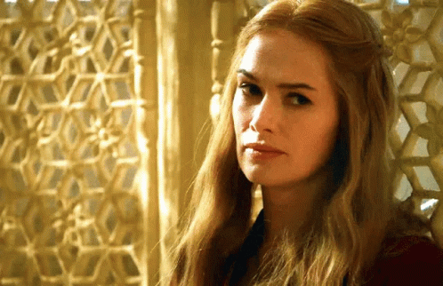 A Woman With Long Blonde Hair Is Sitting In Front Of A Window Looking At The Camera . GIF