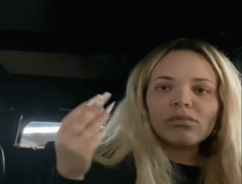 A Woman With Long Blonde Hair Is Sitting In The Back Seat Of A Car And Making A Funny Face . GIF