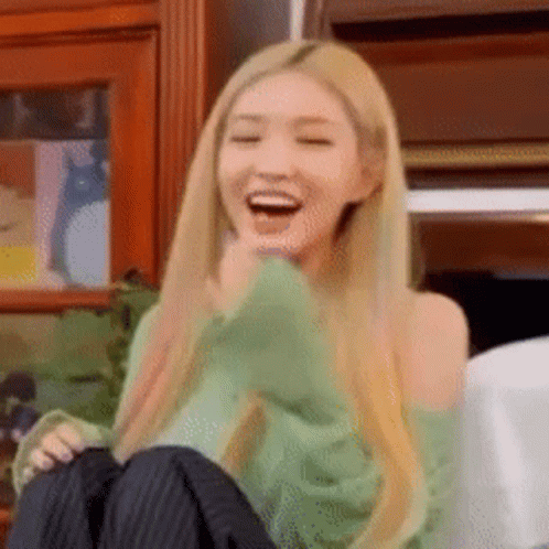A Woman With Long Blonde Hair Is Sitting On A Couch Laughing With Her Mouth Open . GIF