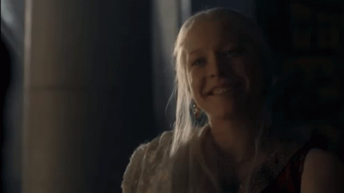 A Woman With Long Blonde Hair Is Smiling And Looking At The Camera . GIF