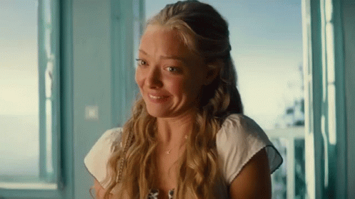 A Woman With Long Blonde Hair Is Smiling And Looking Out Of A Window GIF