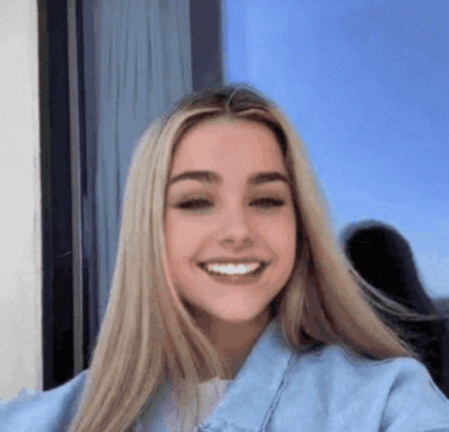 a woman with long blonde hair is smiling for the camera while wearing a blue denim jacket .