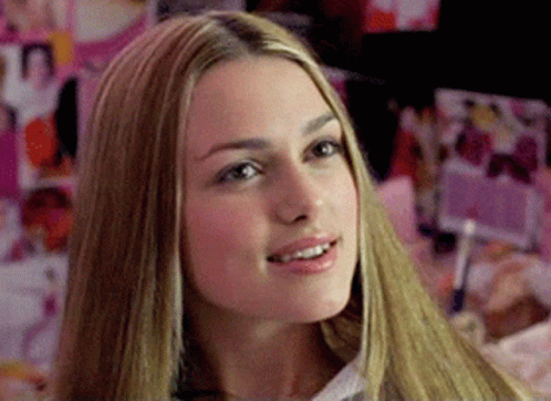 A Woman With Long Blonde Hair Is Smiling In Front Of A Wall Of Pictures GIF