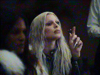 A Woman With Long Blonde Hair Is Smoking A Cigarette In A Dark Room GIF
