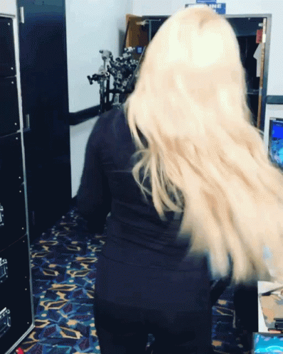 A Woman With Long Blonde Hair Is Standing In A Room With A Sign That Says Airline GIF