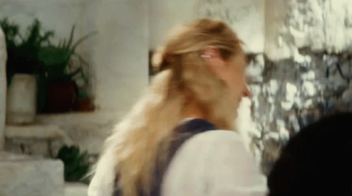A Woman With Long Blonde Hair Is Standing In Front Of A Wall With Pictures On It GIF