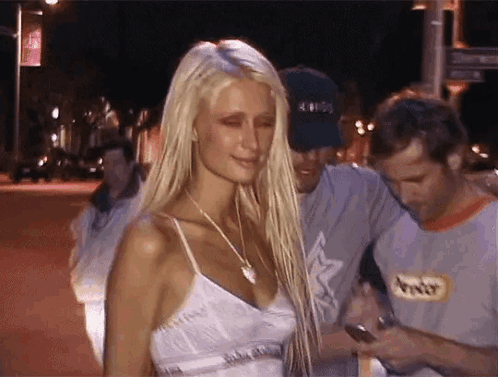 A Woman With Long Blonde Hair Is Standing Next To A Man In A Gray Shirt . GIF