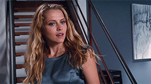 A Woman With Long Blonde Hair Is Standing On A Set Of Stairs Looking At The Camera GIF