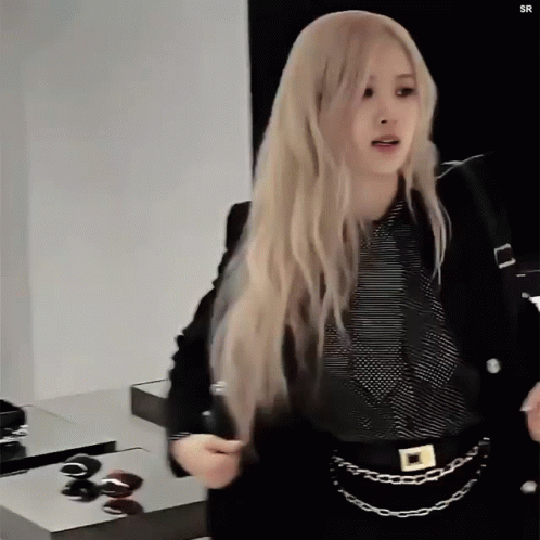 A Woman With Long Blonde Hair Is Wearing A Black Jacket And A Black Striped Shirt . GIF