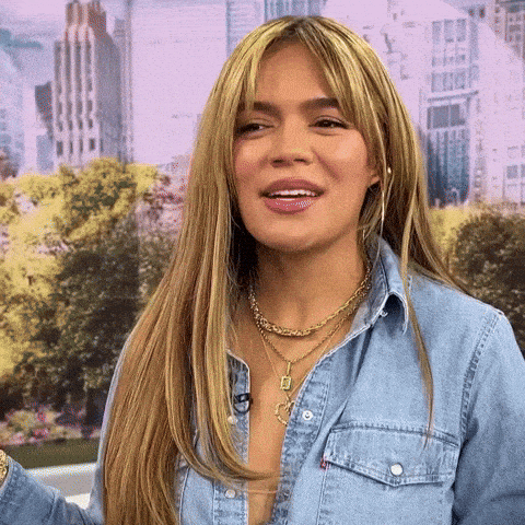 A Woman With Long Blonde Hair Is Wearing A Blue Denim Shirt And A Gold Necklace . GIF