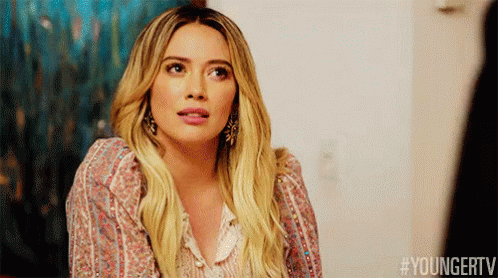 a woman with long blonde hair is wearing a floral shirt and earrings and making a funny face .