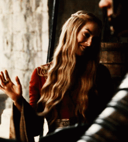 A Woman With Long Blonde Hair Is Wearing A Red Top And A Belt With The Letter S On It GIF