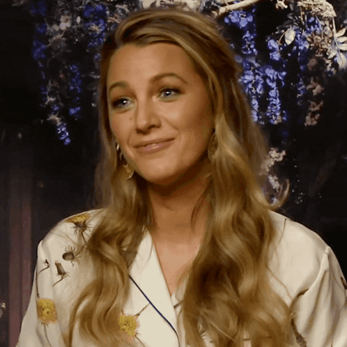 A Woman With Long Blonde Hair Is Wearing A White Robe With Flowers On It GIF