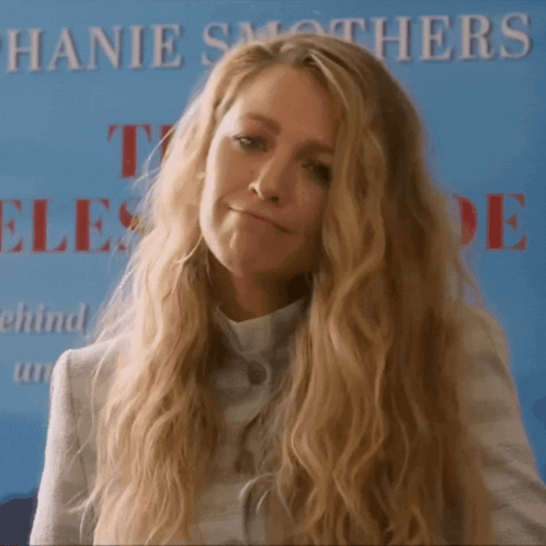A Woman With Long Blonde Hair Stands In Front Of A Sign That Says Hanie Smothers GIF