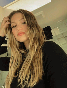 A Woman With Long Blonde Hair Wearing A Black Sweater GIF